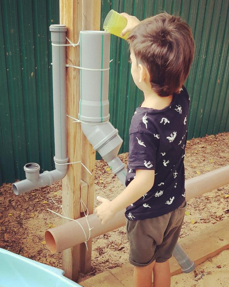 ילד מדגים זרימה של מים בארגז החול בגן